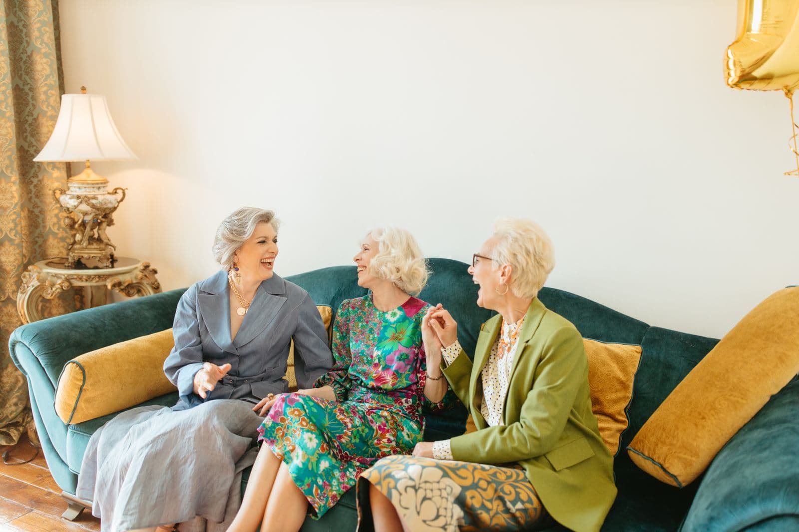 Three older women laughing together on a sofa