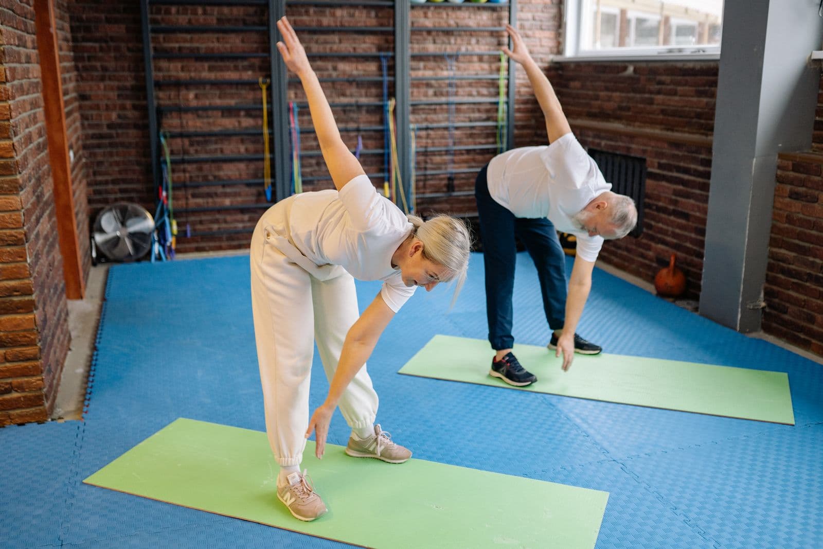 Older couple stretching on exercise mats in a bright gym