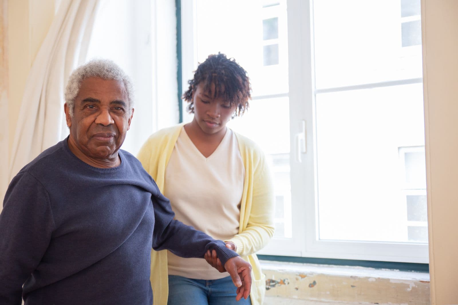 Caregiver helping an older man stand up from his armchair at home