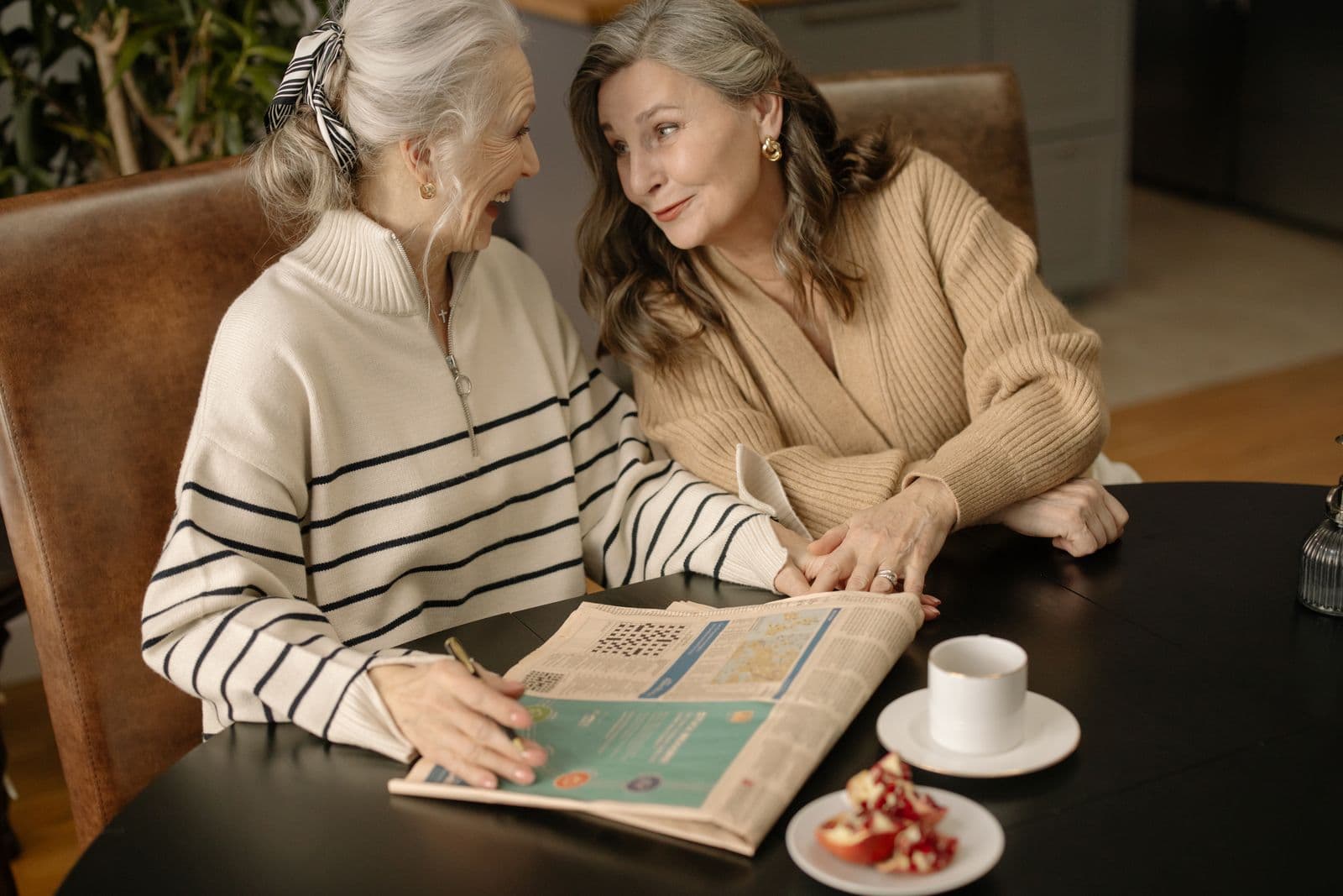 Two older women laughing together over a crossword puzzle