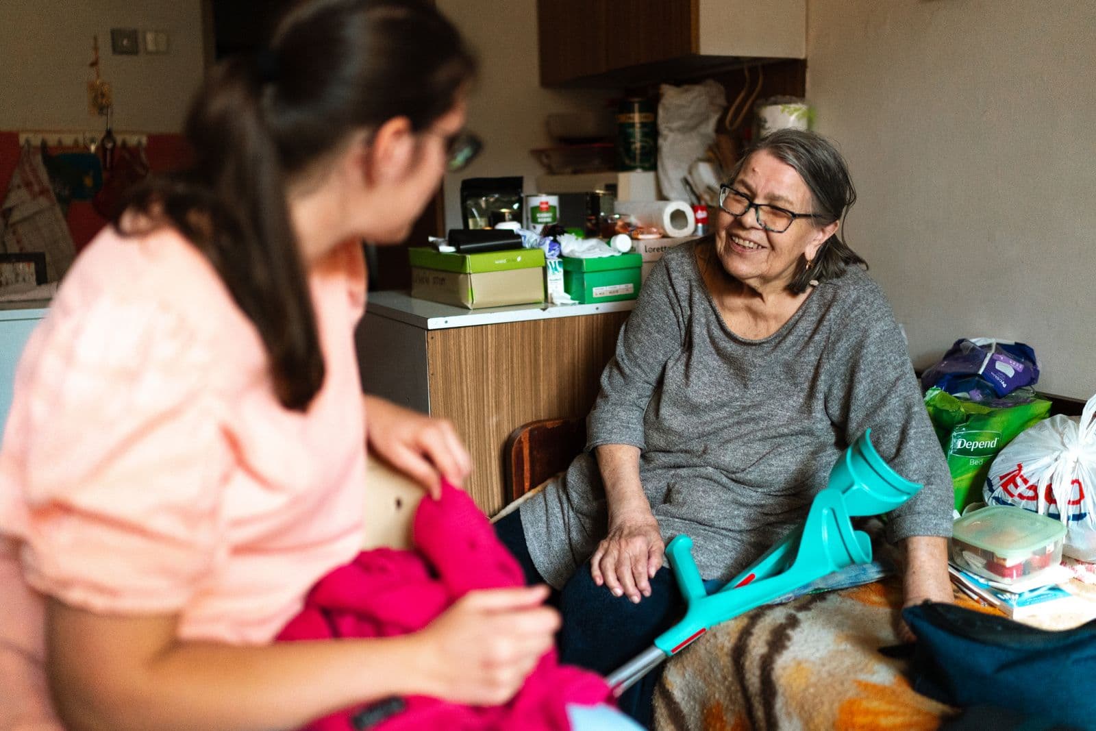 Caregiver sitting with an older woman and helping her with a task at home
